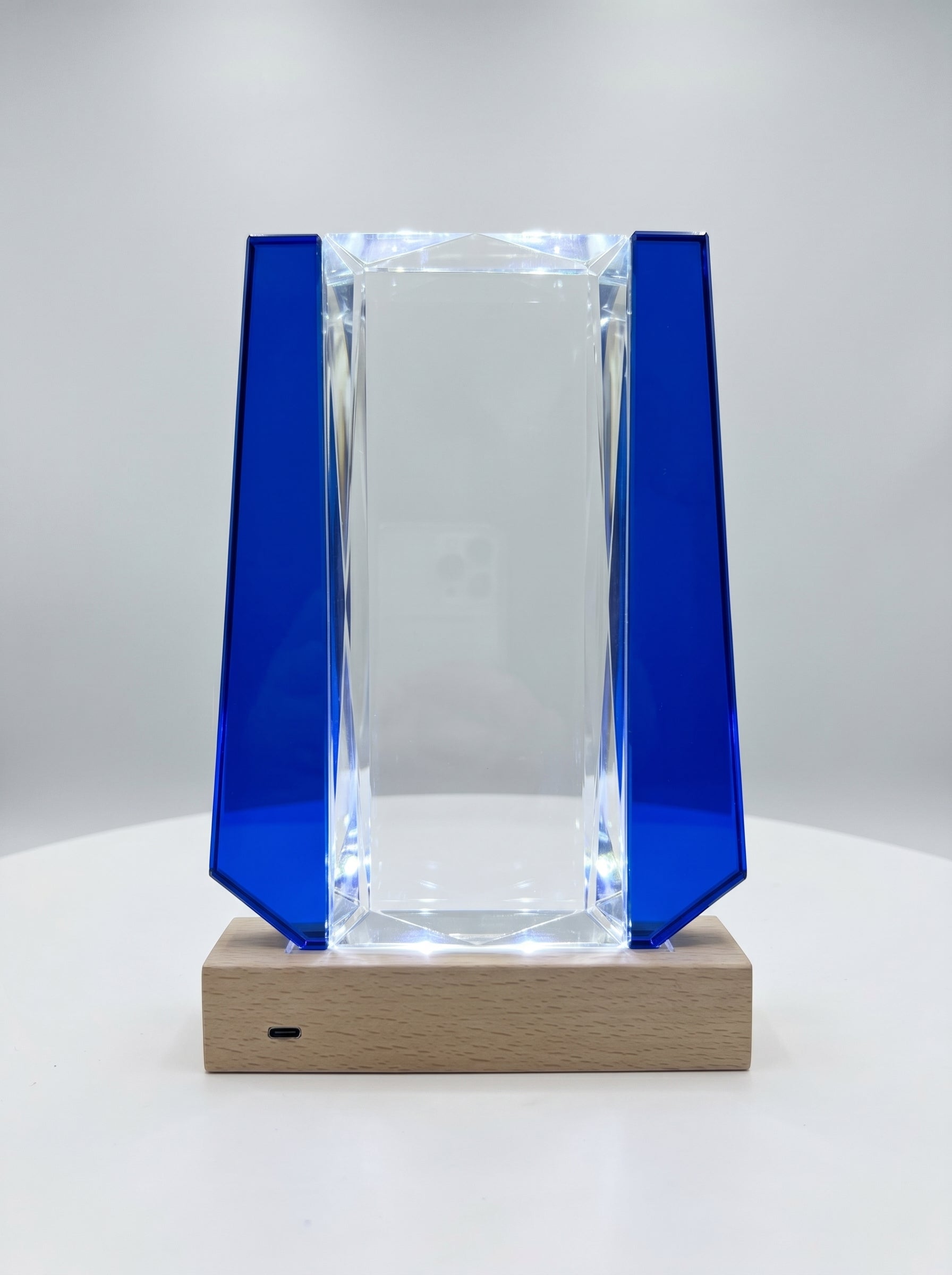 Trophée verre lumineux à facettes biseautées avec ailes bleu cobalt sur socle bois éclairé.
